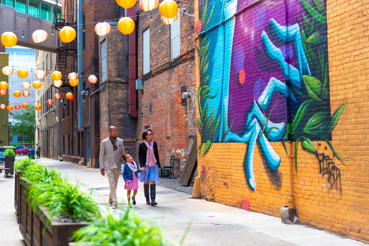 Father, mother, and daughter walking past a mural and the Porch off Calhoun in downtown Fort Wayne, Indiana.