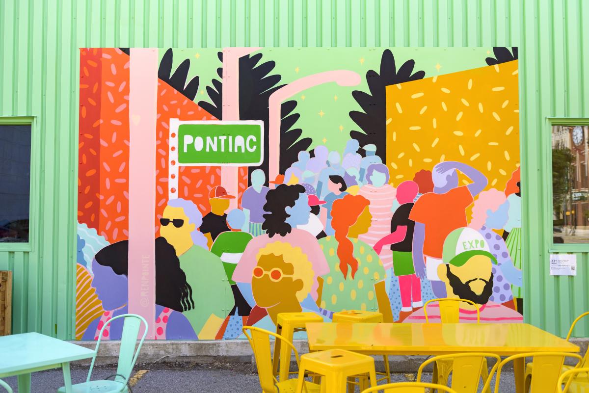 Colorful mural on the side of a mint green building showcasing a depiction of the Pontiac Street Black Expo