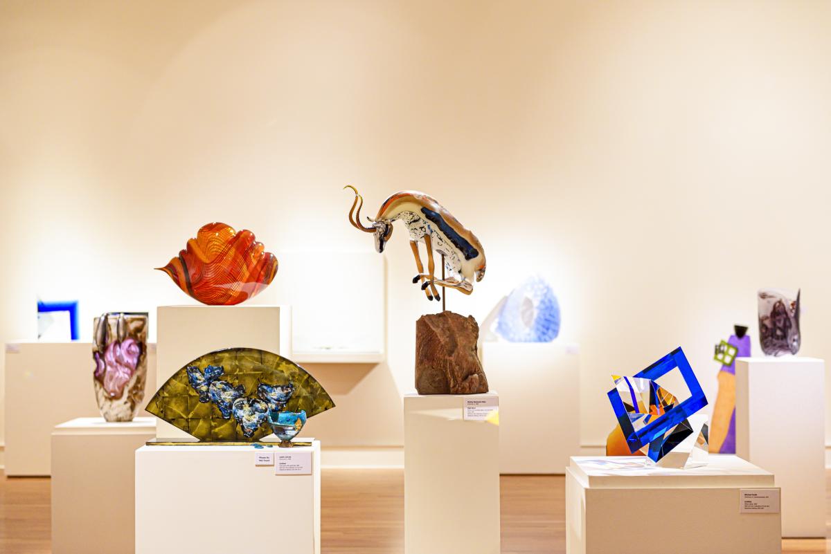 Colorful glass art sculptures displayed in a modern gallery setting at the Fort Wayne Museum of Art, featuring vibrant lighting and reflective surfaces.