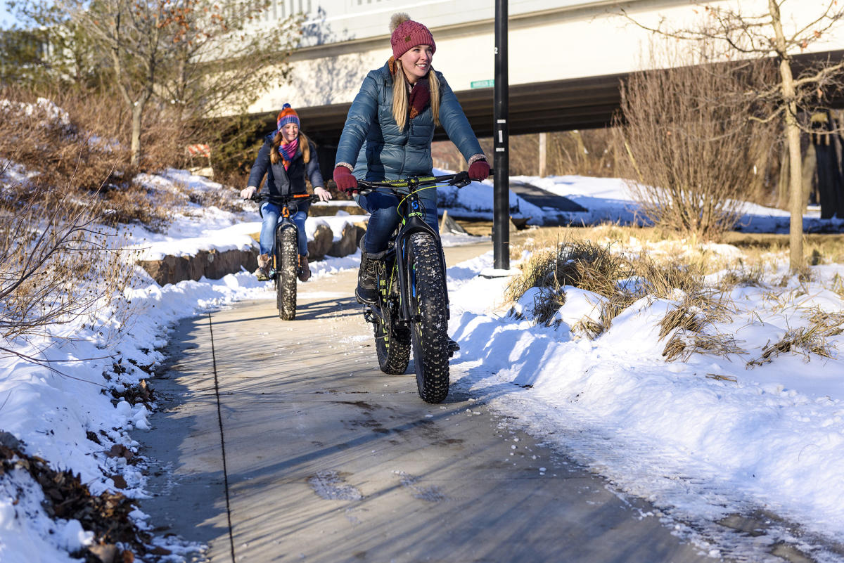two girls on fat tire bikes on a sidewalk surrounded by snow