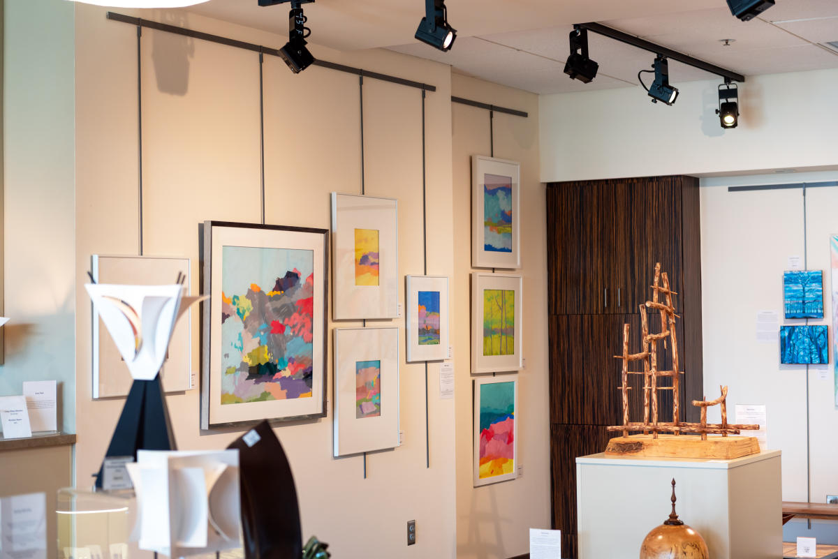 Interior of the Paradigm Gallery gift shop at the Fort Wayne Museum of Art. Fine art paintings hang on the wall and several small sculpted pieces are displayed in the middle of the room.