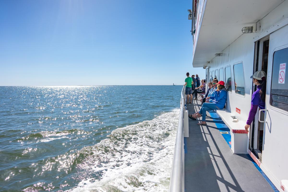 A group of people sitting on a ferry watching the blue water.