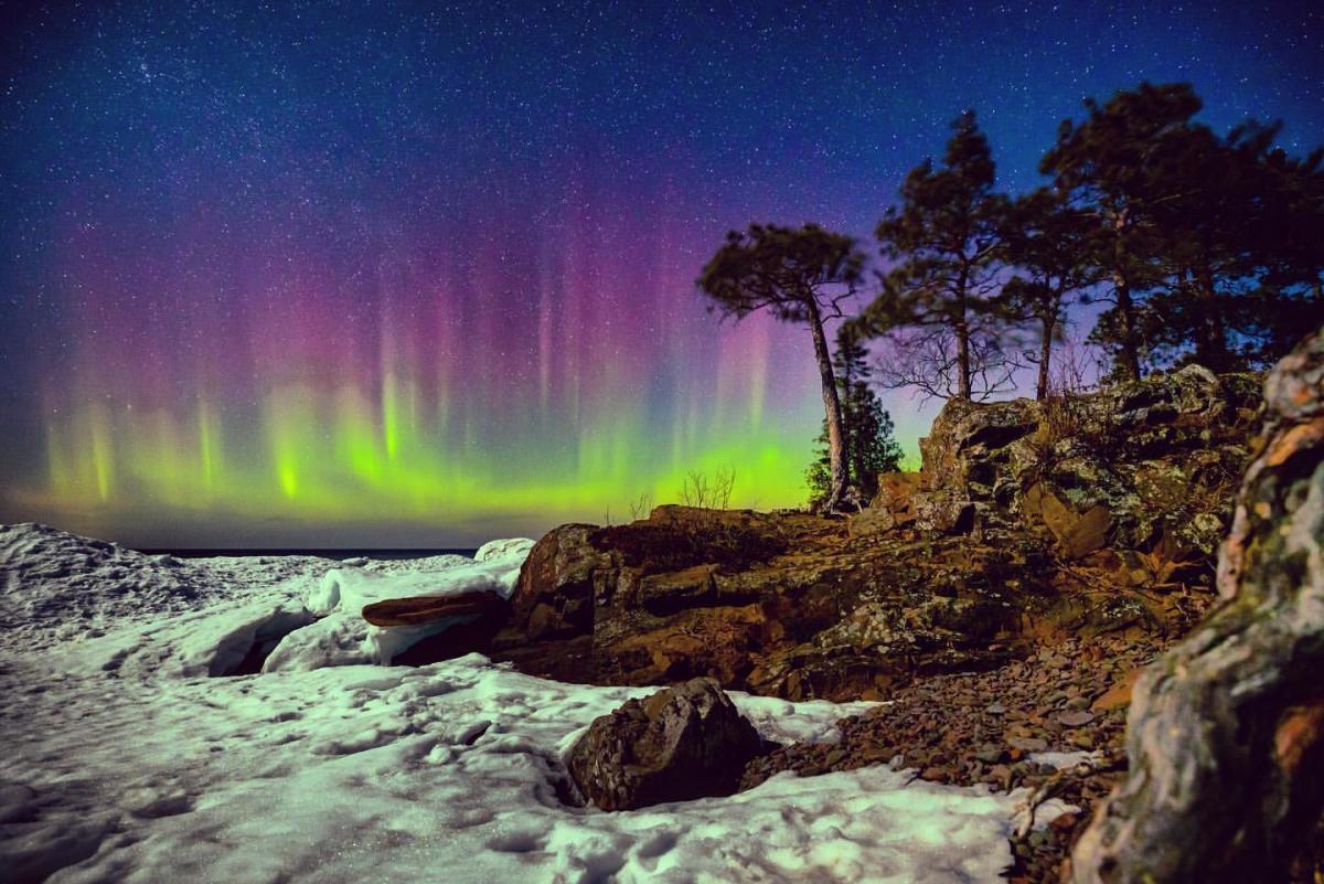 Pinks, purple, and green Northern Light Columns in the sky over Lake Superior's frozen shoreline
