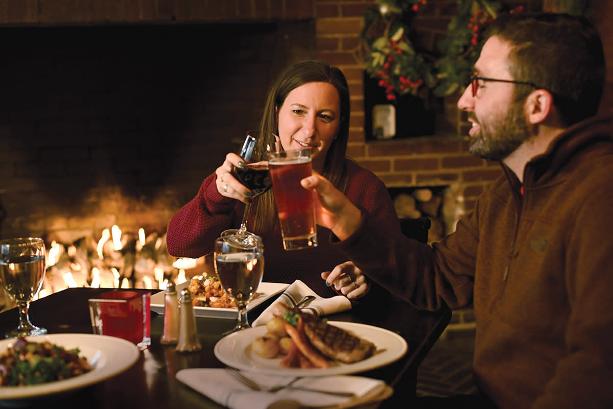 A couple enjoying dinner and drinks by a fireplace in a restaurant