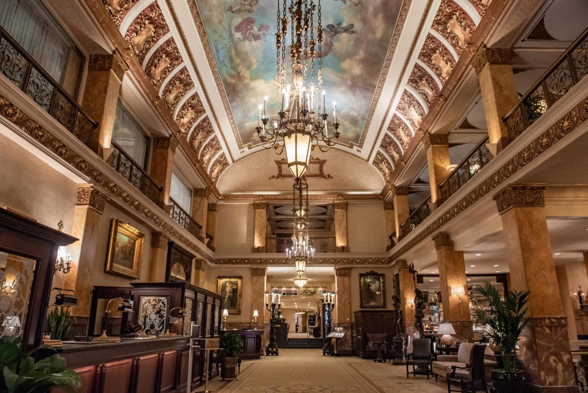 Grand hotel lobby with ornate chandeliers, marble columns, and a painted ceiling mural, creating an elegant and historic atmosphere.