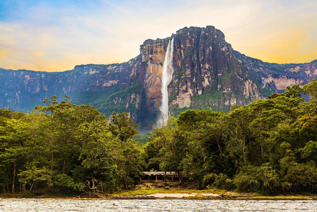 A towering waterfall, known as Angel Falls in Venezuela, plummets from a flat-topped mountain, surrounded by lush, green jungle.