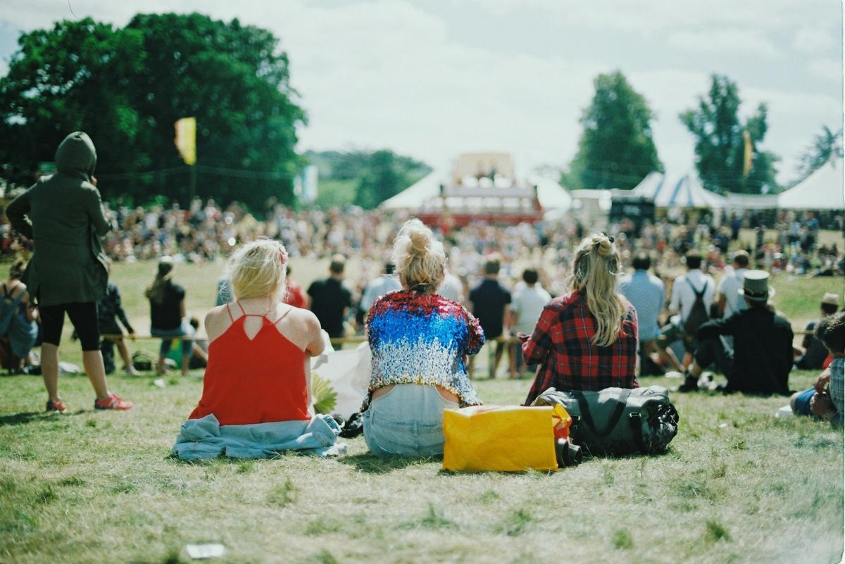 Three people sitting watching a festival tent in the distance