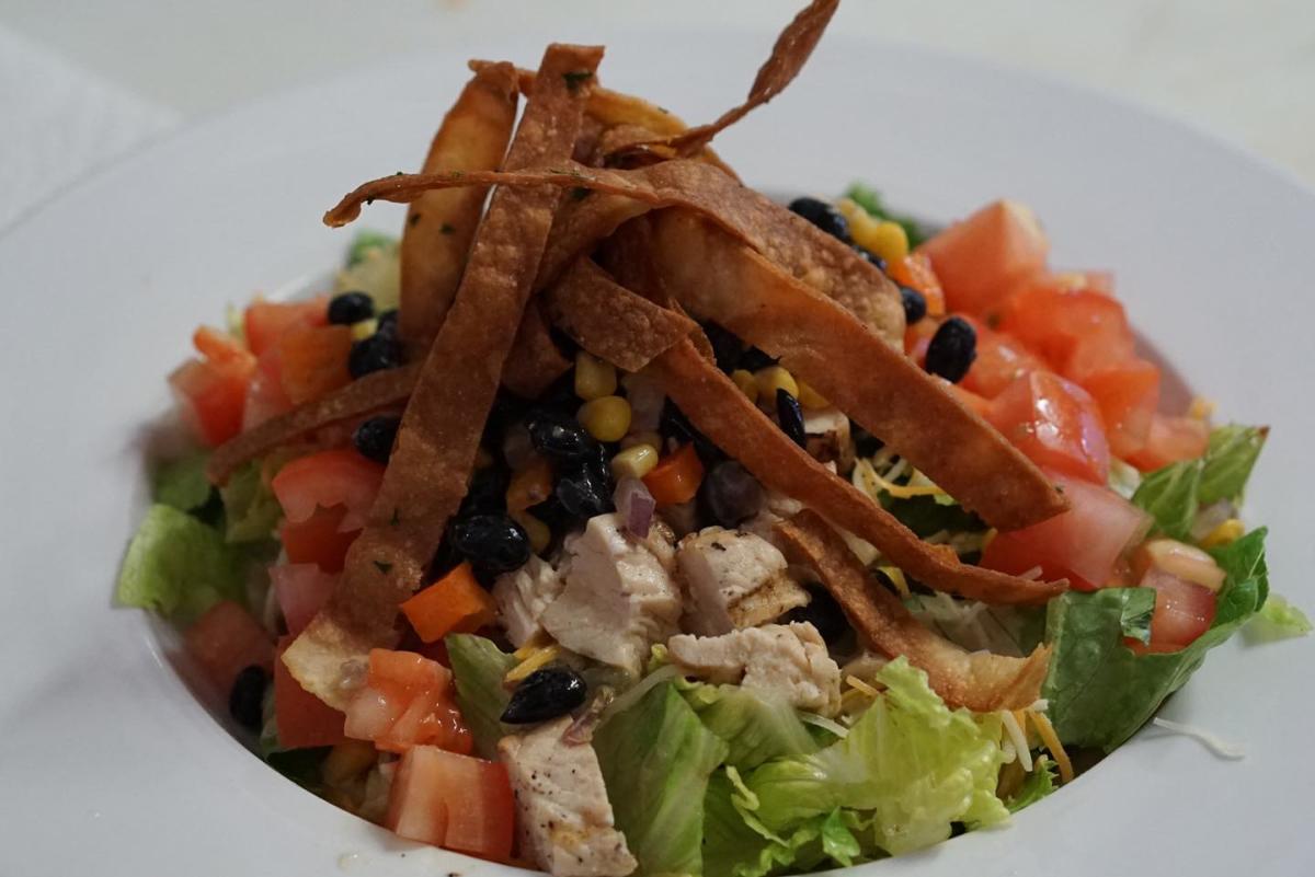 Fresh green lettuce is topped with chicken, corn, tomatoes, black beans and wonton strips to create the BBQ Ranch Chicken Salad at The Kitchen