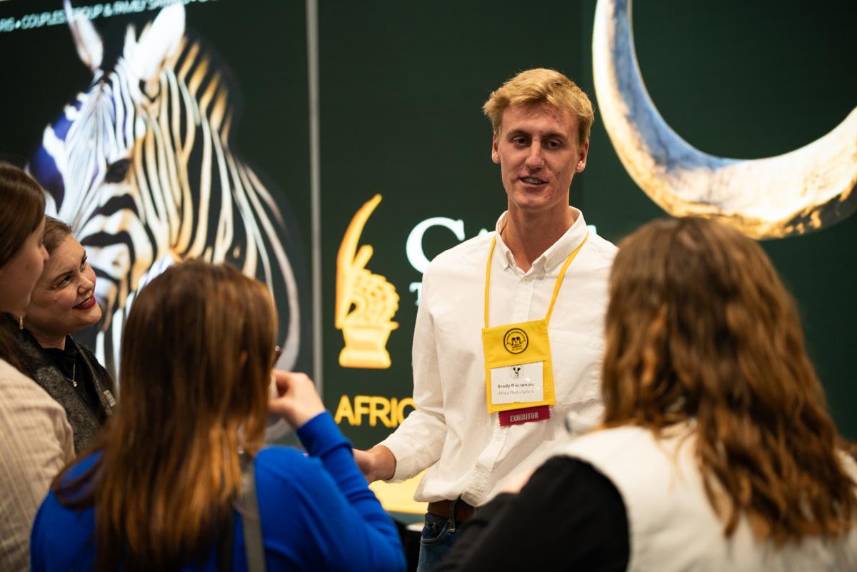 Exhibitor Brody Nieuwoudt discusses his African Photo Safari with four women at his booth during the Houston Safari Expo.