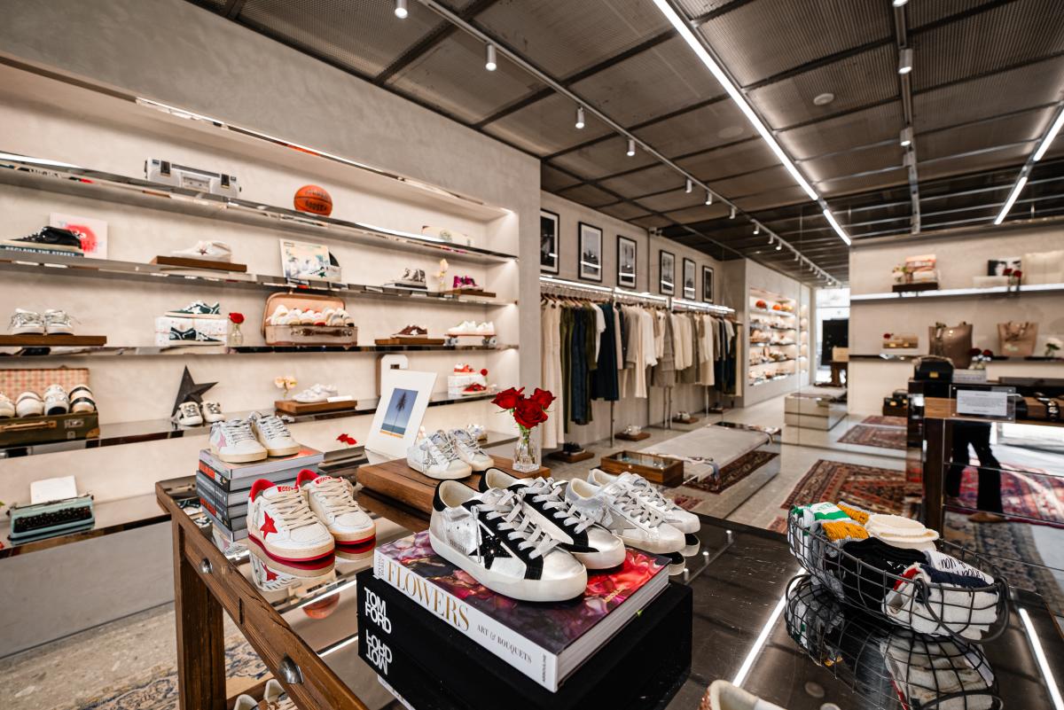 An overview of The Golden Goose Boutique on Market Street. A table near the camera features matching "distressed" sneakers in different colors, all with glitter or sequin accents. Some are raised or propped up with coffee table books. Along the back wall are more shoes, some staged with or tucked into various vintage items: suitcases, records, skateboards, etc.