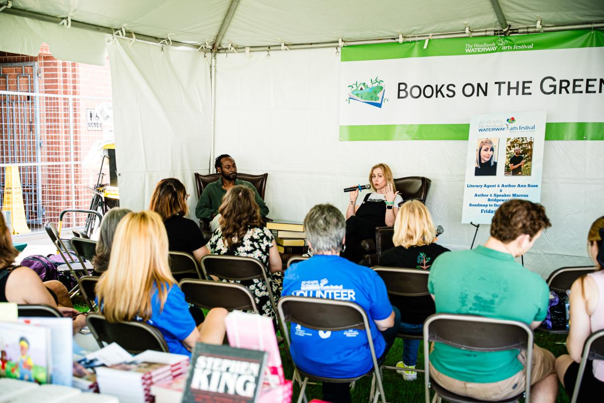 An audience sits in fold-out chairs to listen to authors...