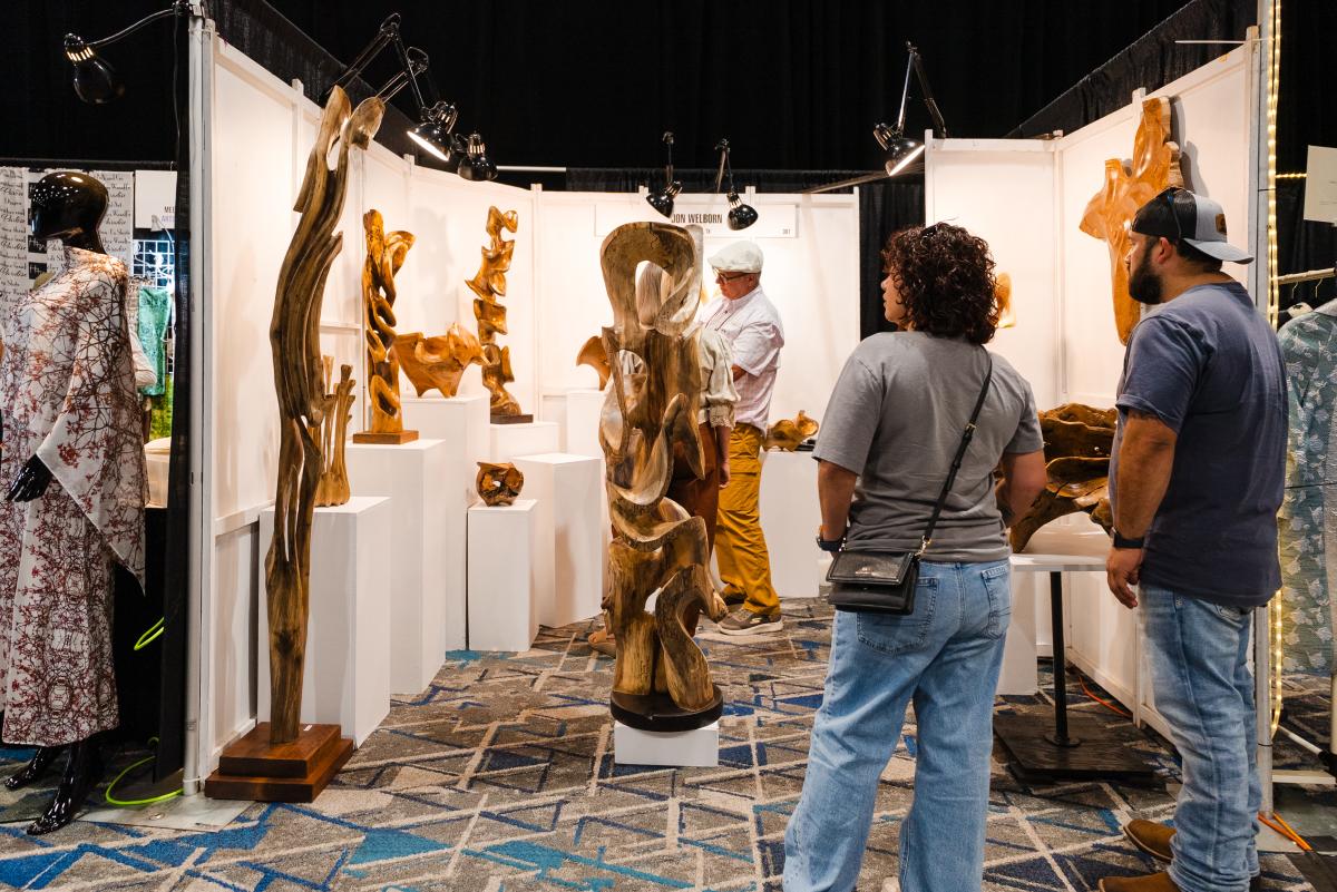 A Latino couple admires Jon Welborn's wood sculptures at the 2026 Texas Fine Craft Show.