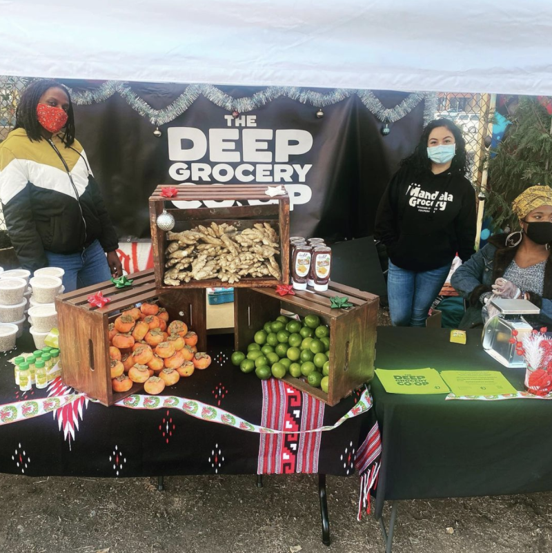 Woman working at the DEEP Grocery COOP stand with produce on display