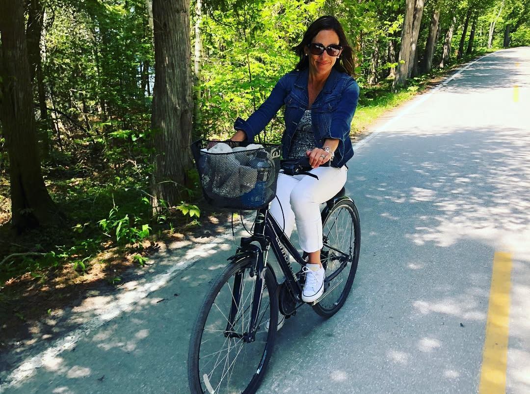 A woman pedals a bicycle with a basket down a road on Mackinac Island