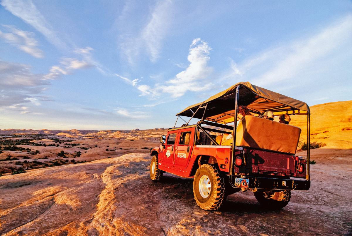 An open-air red Hummer 4x4 on the sandstone slickrock of the Hell's Revenge trail during a guided sunset off-roading in Moab, Utah.