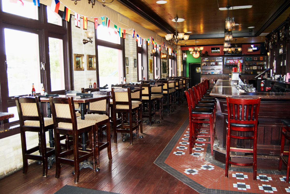 Interior of Red Lion Pub with tall windows, a long wooden bar lined with red stools, high-top tables and international flags hanging from the ceiling.