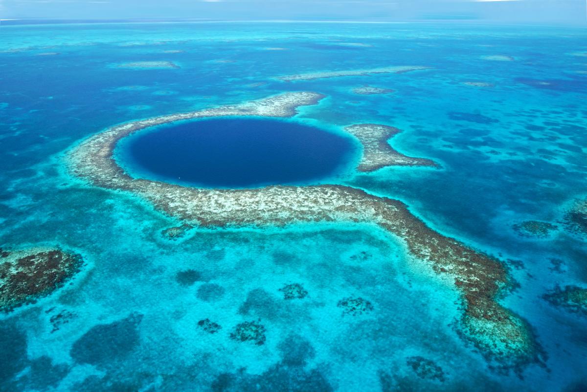 Aerial view of the Great Blue Hole, a massive circular underwater sinkhole surrounded  by vibrant coral reefs in the Belize Barrier Reef.