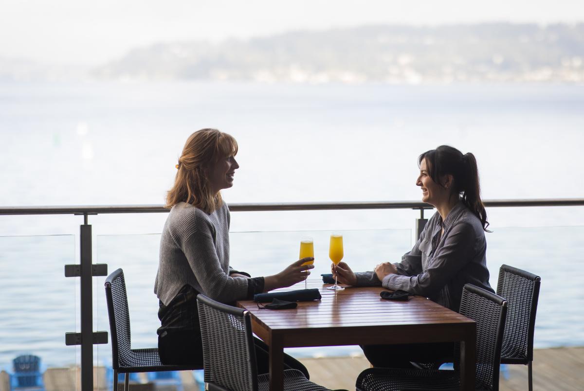 Two guests enjoying drinks at a waterfront restaurant patio overlooking Lake Washington, with scenic lake views and outdoor dining in Renton.