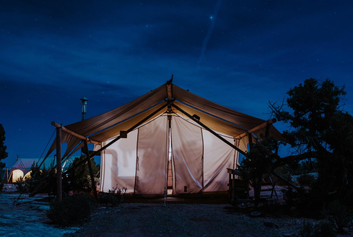 A safari-style canvas tent at Under Canvas Moab glowing at night.