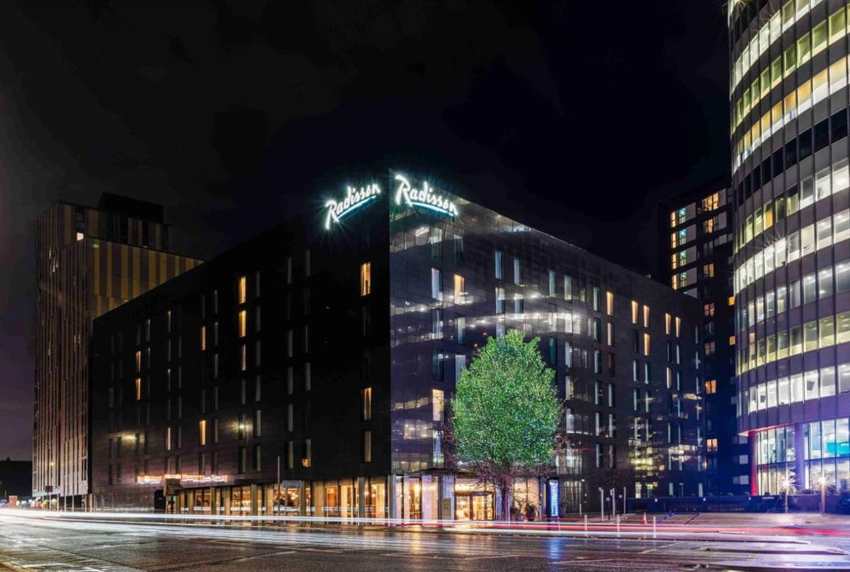 Exterior view of Radisson Manchester City Centre illuminated at night, with the hotel signage visible and modern city buildings surrounding the property.
