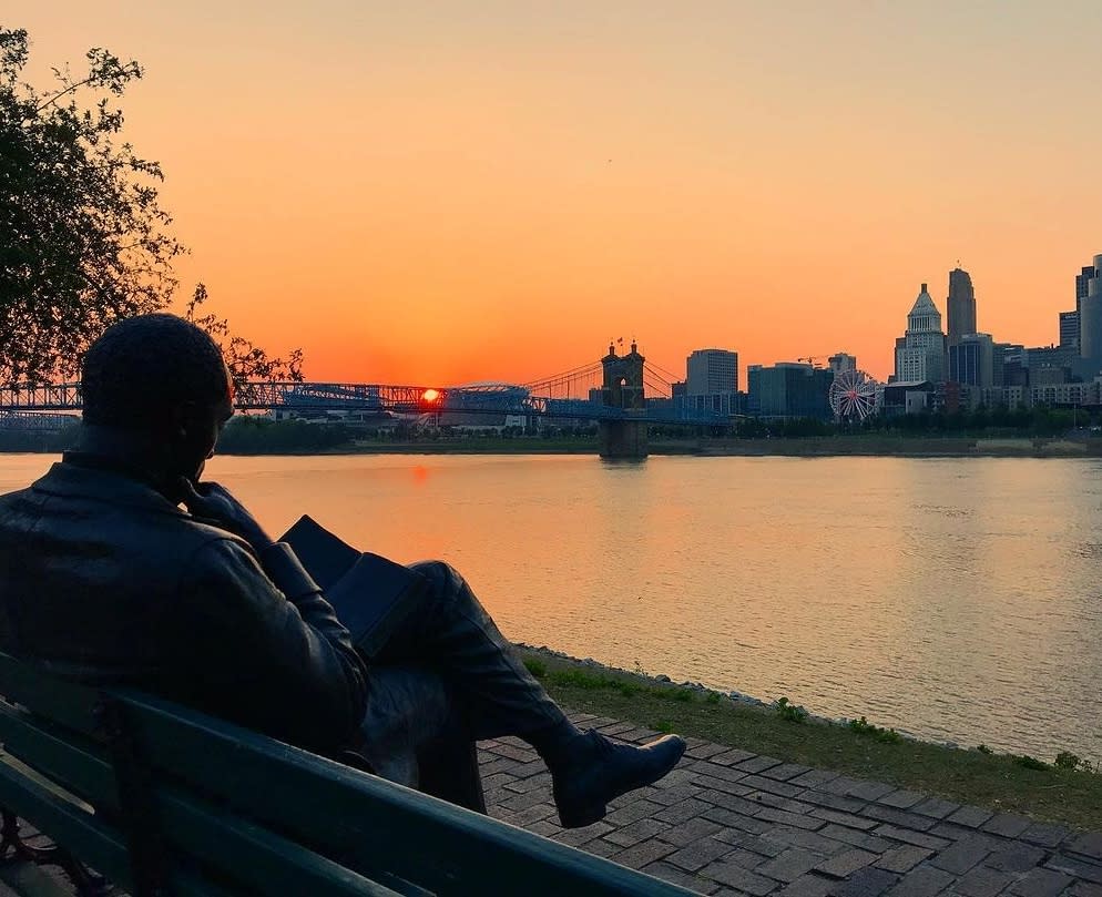 James Bradley statue seen from behind, looking at sunset behind the Roebling Bridge
