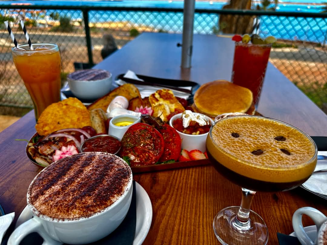 A range of food and drinks on a table at SOAK Cafe in Dampier with a view of Hampton Harbour in the background