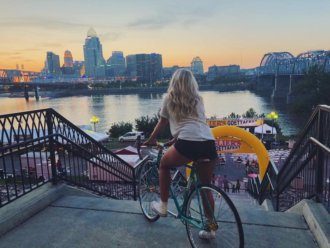 A young woman on a bicycle looks out over Goettafest in Newport, Ky. and the Cincinnati skyline in the background
