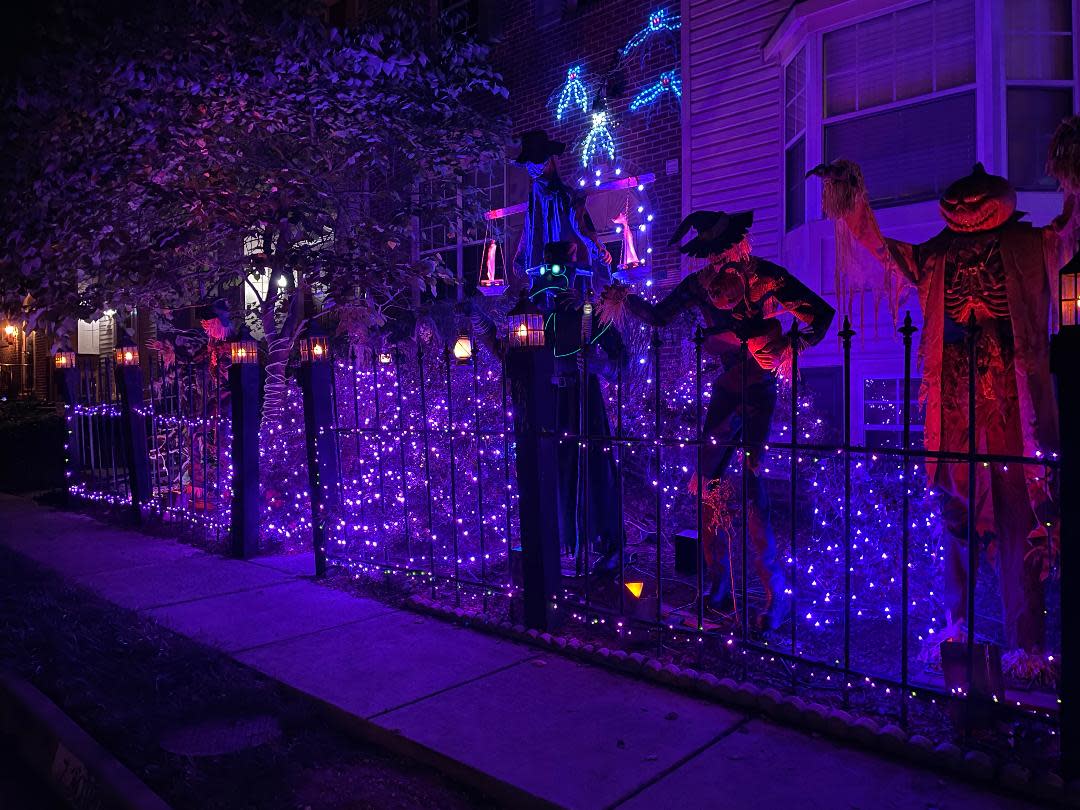 Lit up front of townhouse draped in purple glowing lights. Huge animatronic scarecrows, pumpkin skeletons, and glowing insects loom over the walkway.