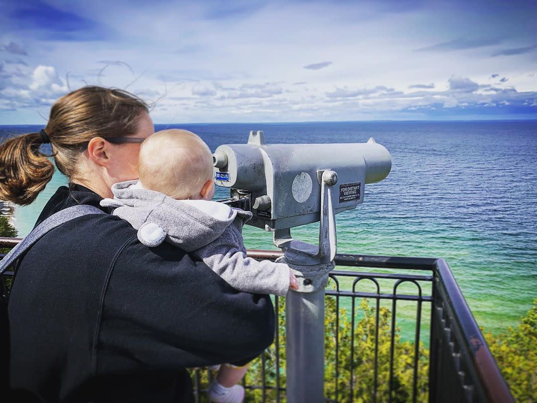A baby held by a woman looks through a tower viewer on a Mackinac Island observation platform