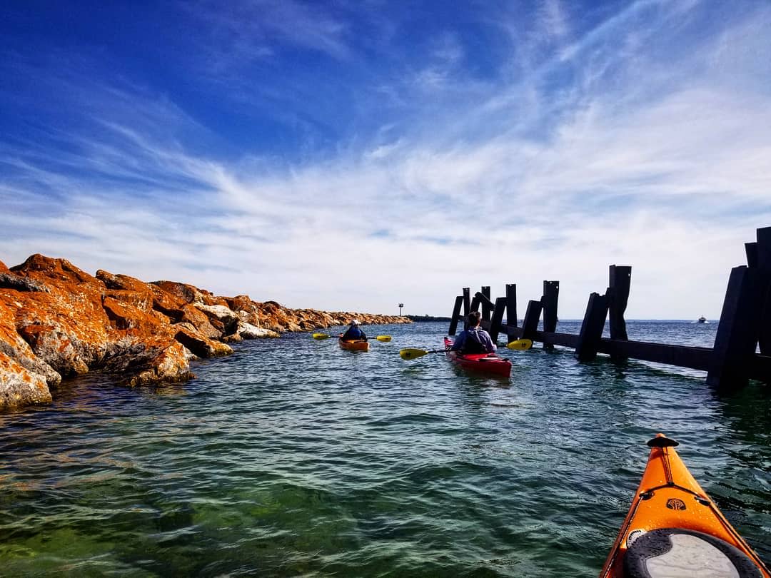 Kayakers paddle along a rock wall in the water off Mackinac Island