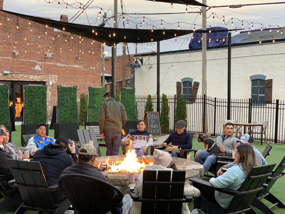 A group of people enjoying drinks around a fire pit at Fall Line Brewing Co