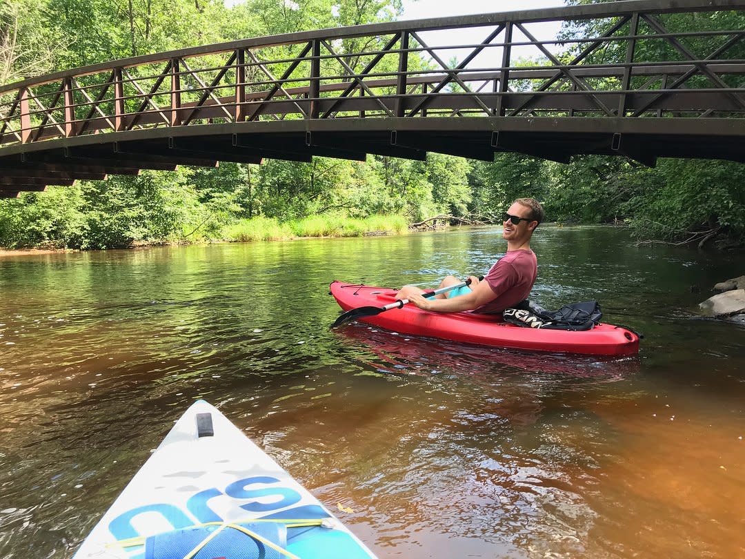 A kayaker enjoys the meandering Plover river and passes under a copper bridge.