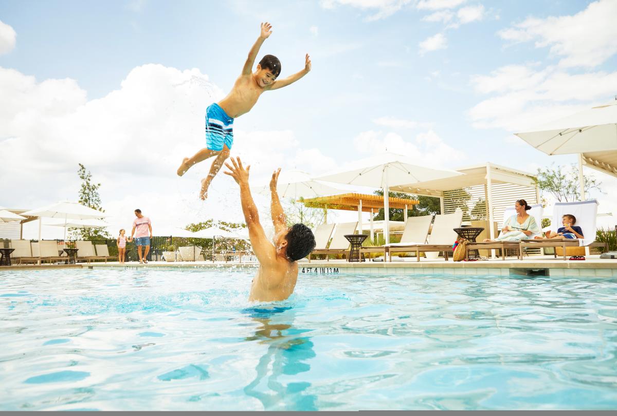 A boy jumping into the pool where his dad is waiting to catch him.