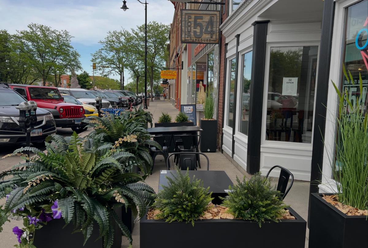 The outdoor patio of Pour 54 in downtown Rapid City, featuring all-black tables and chairs surrounded by green plants in black planter boxes.