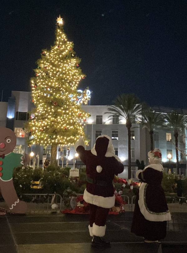 Image of Christmas tree lit up with Santa Claus and Mrs. Claus standing in front.