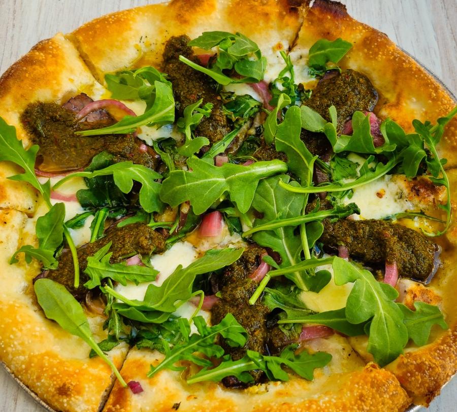 A small pizza with chimichurri steak, fresh arugula, red onions, and cheese
