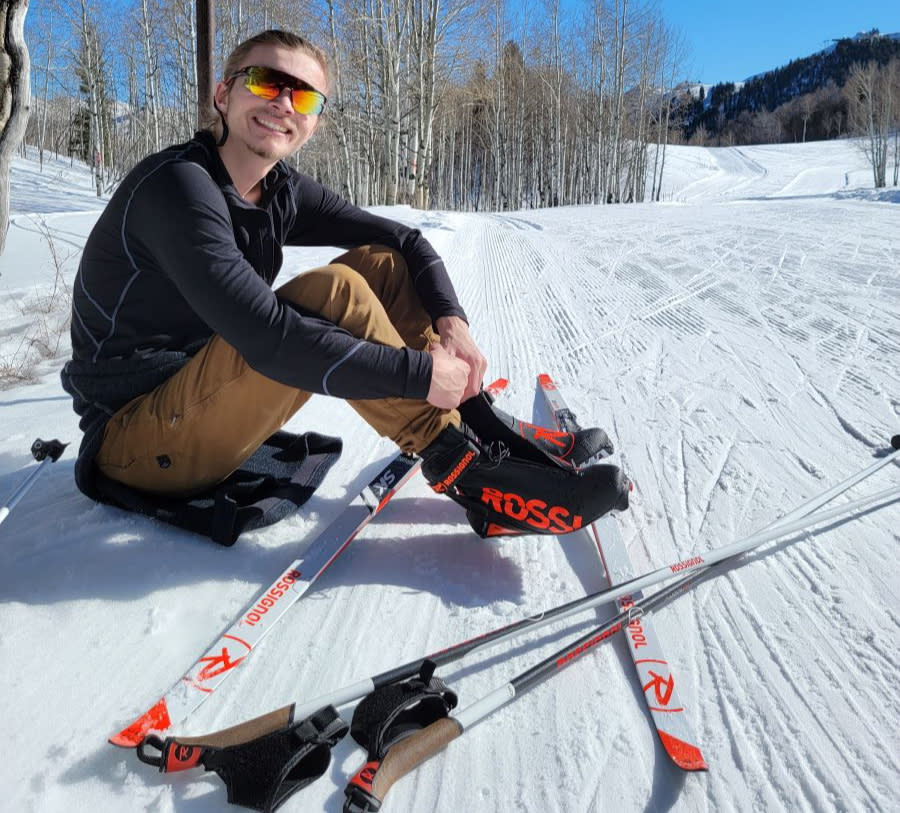 young man sits on side of skate ski trail with skis on