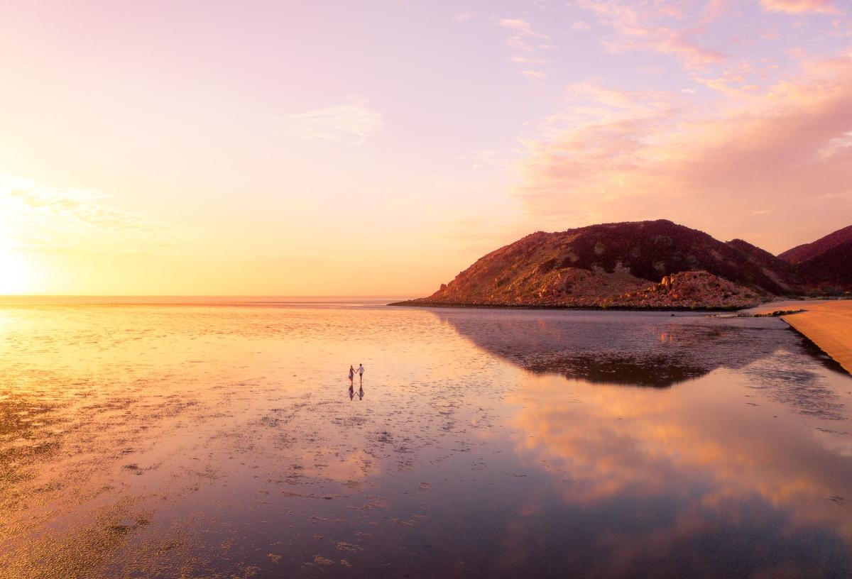 A couple walks on the beach at sunset at low tide, Hearson's Cove in the Pilbara, Western Australia