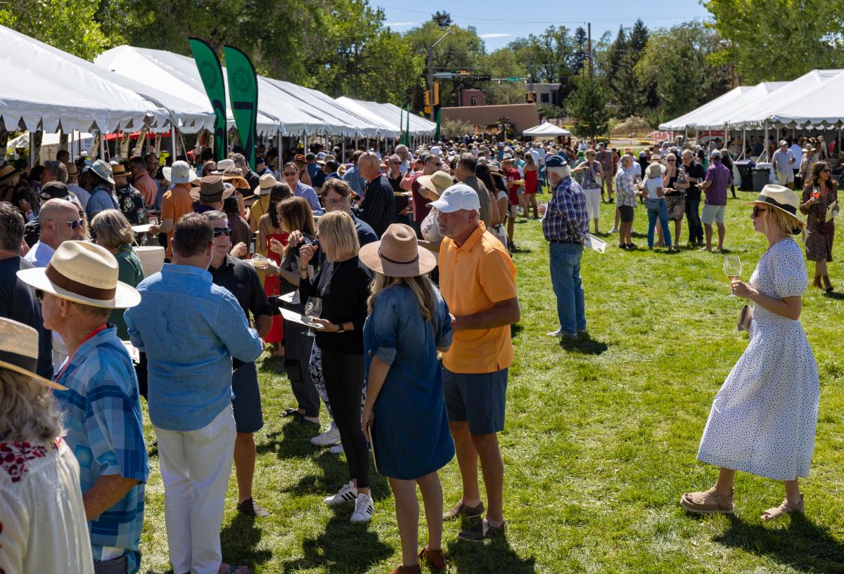 A large group of people stand in a green field surrounded by white tents