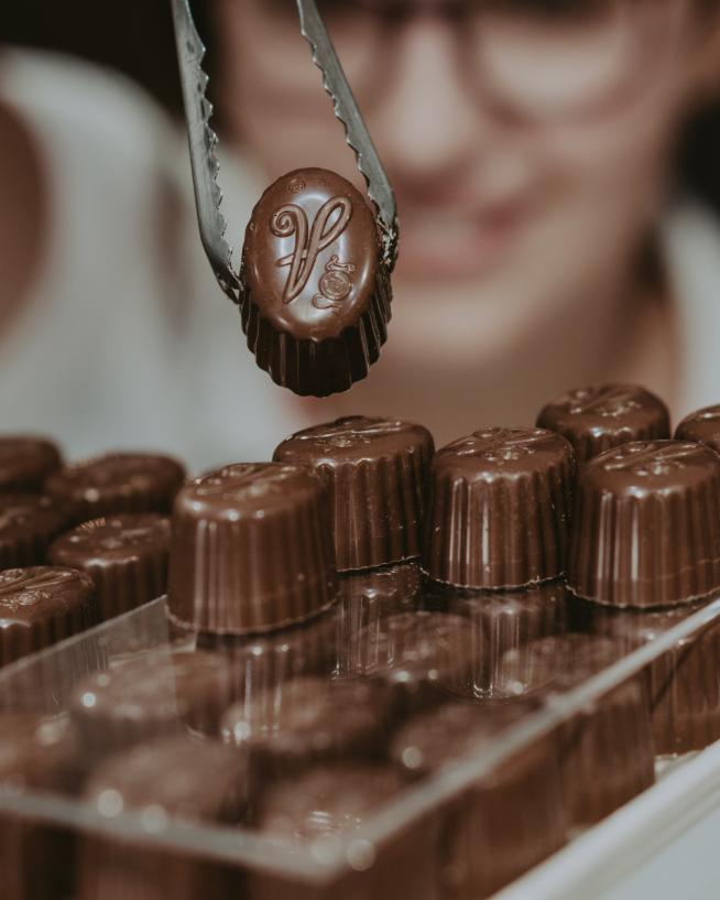 A woman picks a truffle from an array of chocolates.