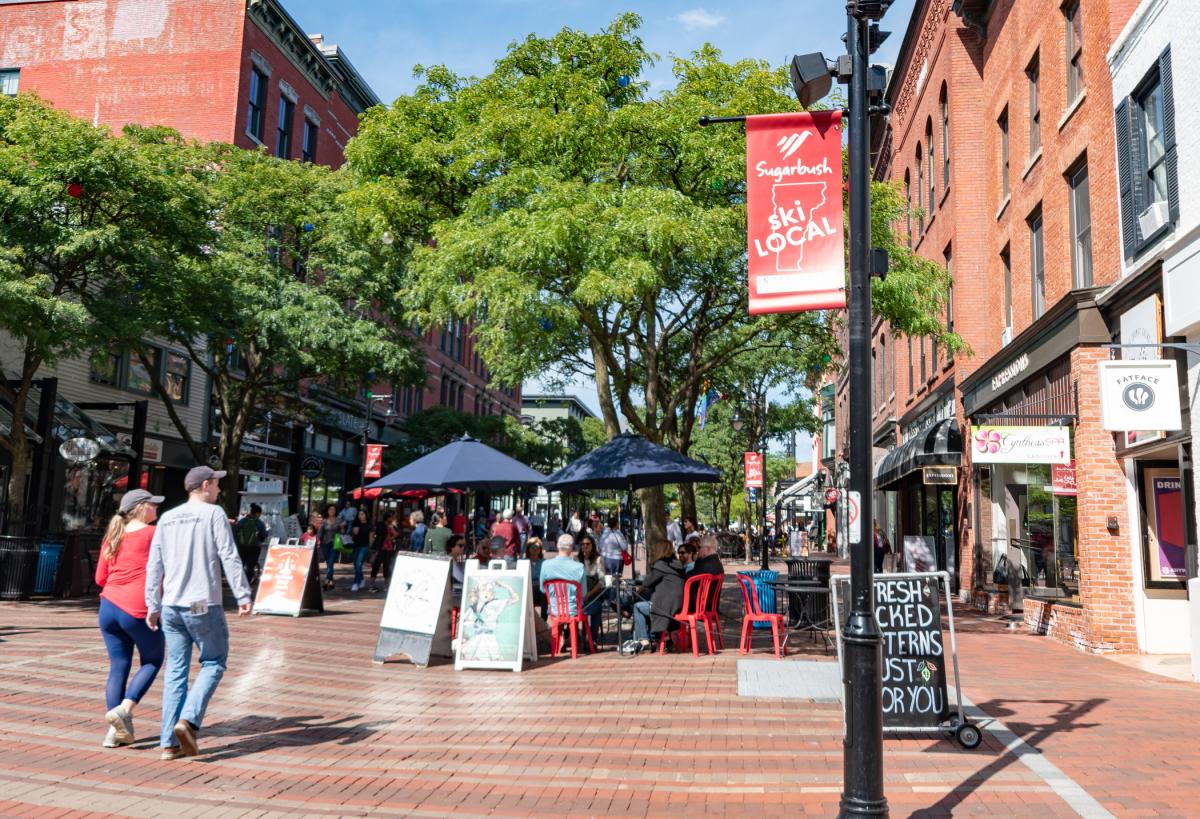 A sunny day on Church Street. People are out walking and enjoying outdoor restaurant seating under umbrellas.