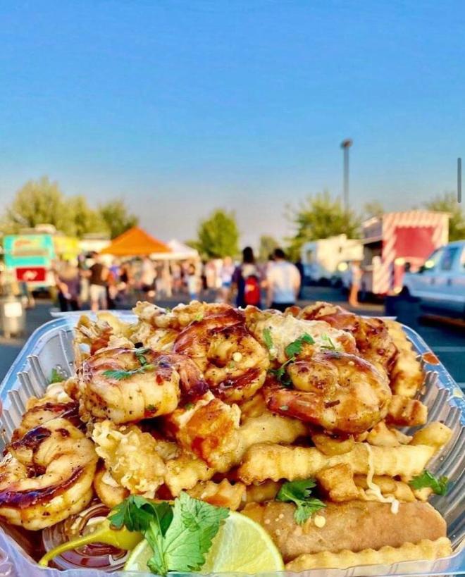 Plate of fries covered in shrimp and cheese with food trucks in the background