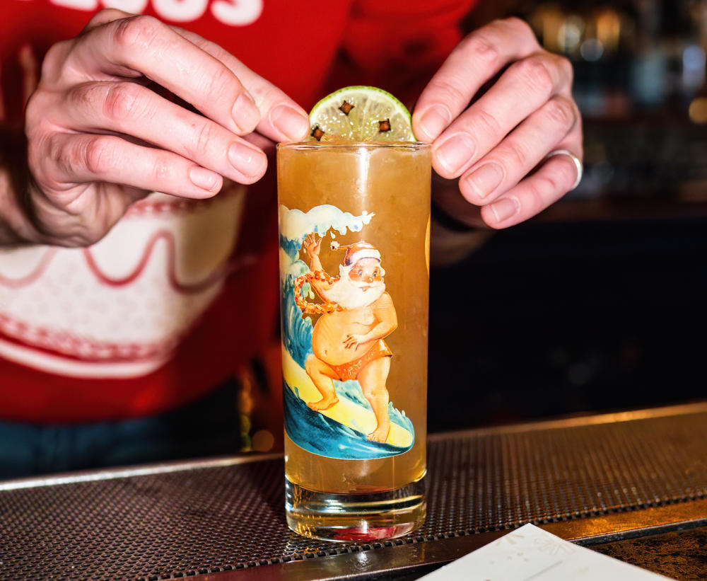 Bartender garnishing a glass with a printed surfing santa