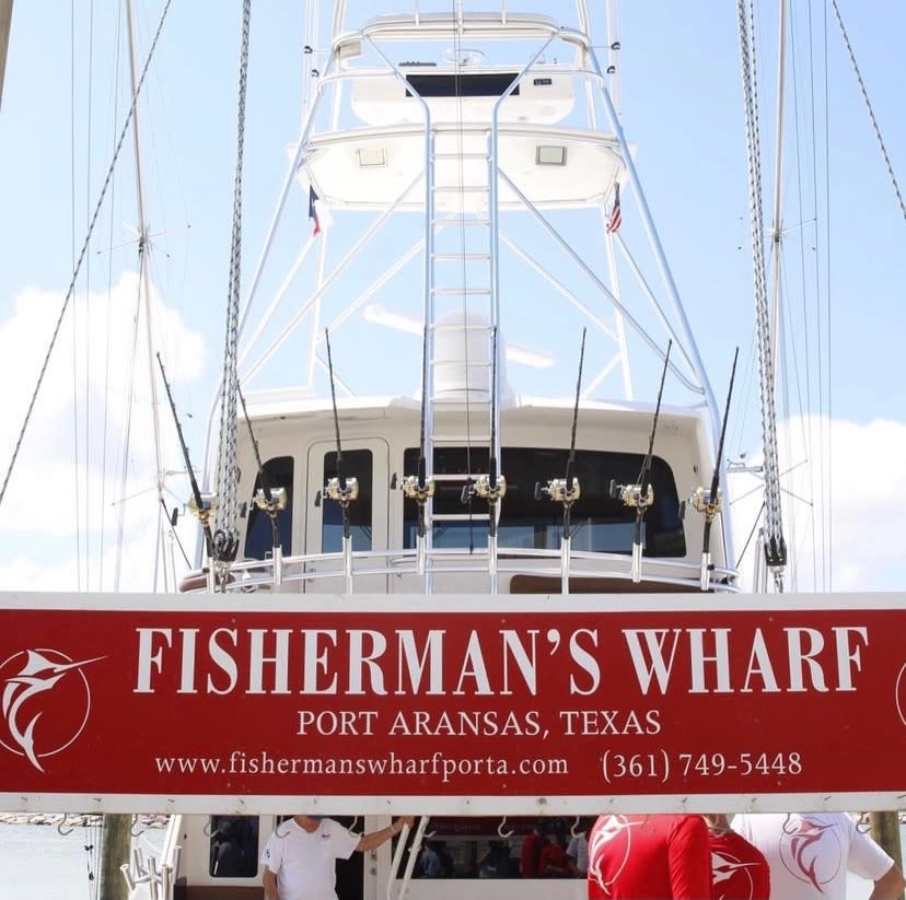 A large white fishing boat is behind a red sign that reads "Fisherman's Wharf Port Aransas."