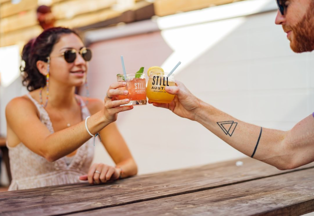 Image of a man and women holding their cocktails together on the patio at Still Austin Whiskey Co.