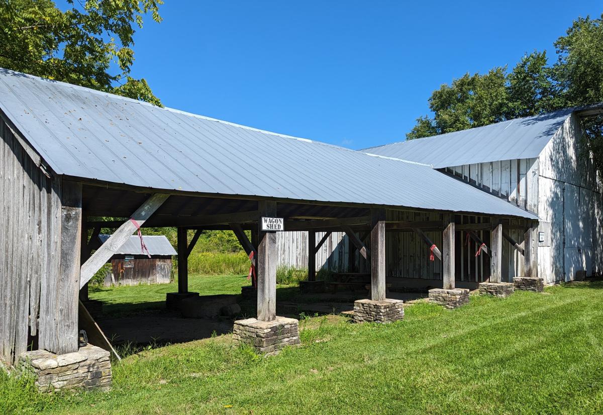 Image is of a barn on the far right and an open air garage structure with 4 openings.