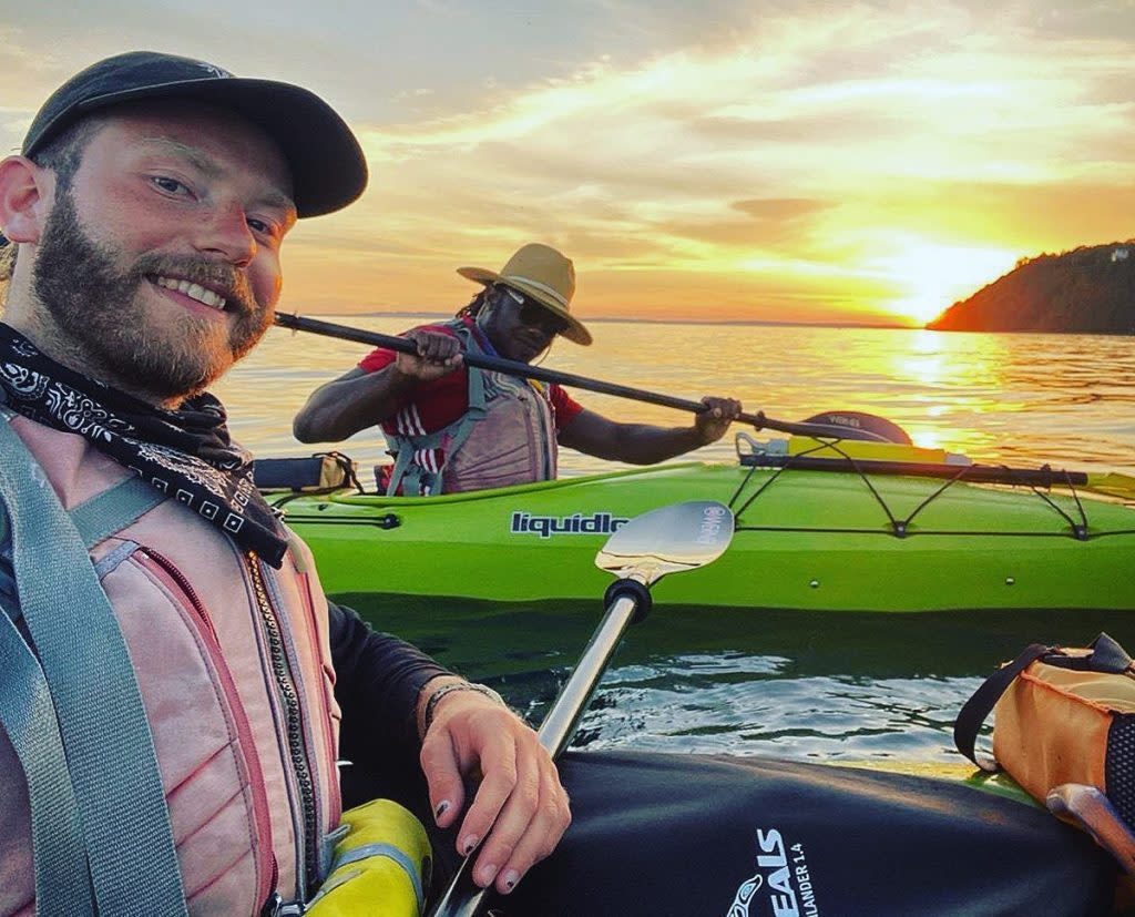 Two guys paddle kayaks at sunset in the water off Mackinac Island
