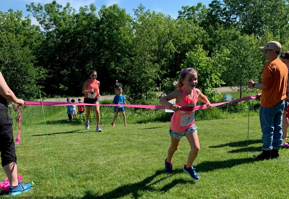 A young girl cheers as she crosses the 5K finish line in the park.