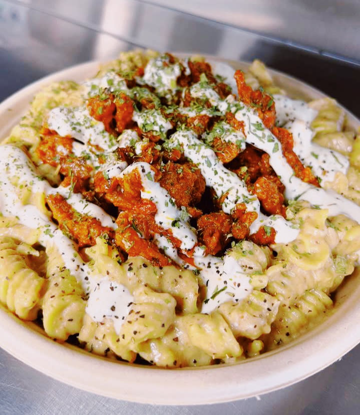 A bowl of Mac and cheese with red sauce and white drizzle on top