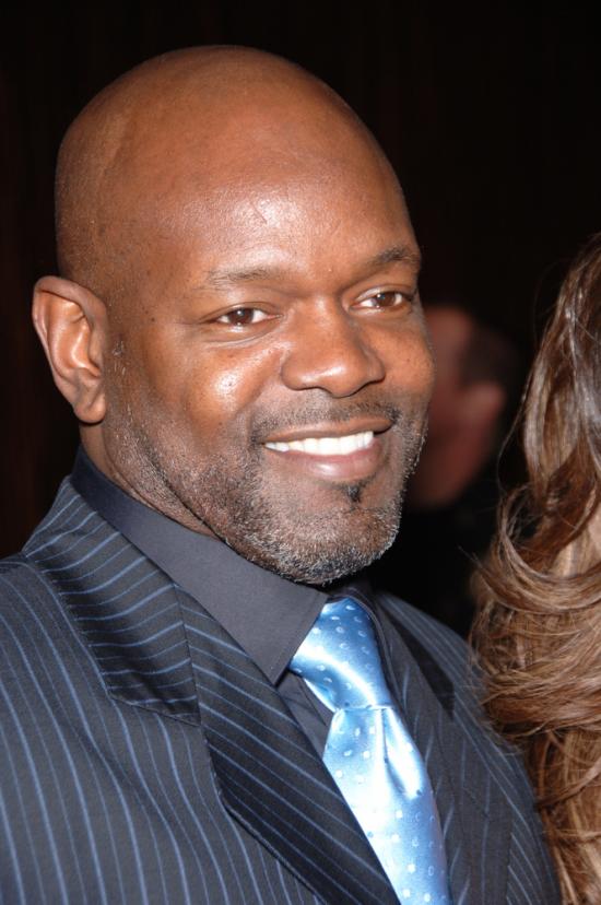 Emmitt Smith smiling wearing a gray pin-striped suit and Dallas Cowboys blue tie